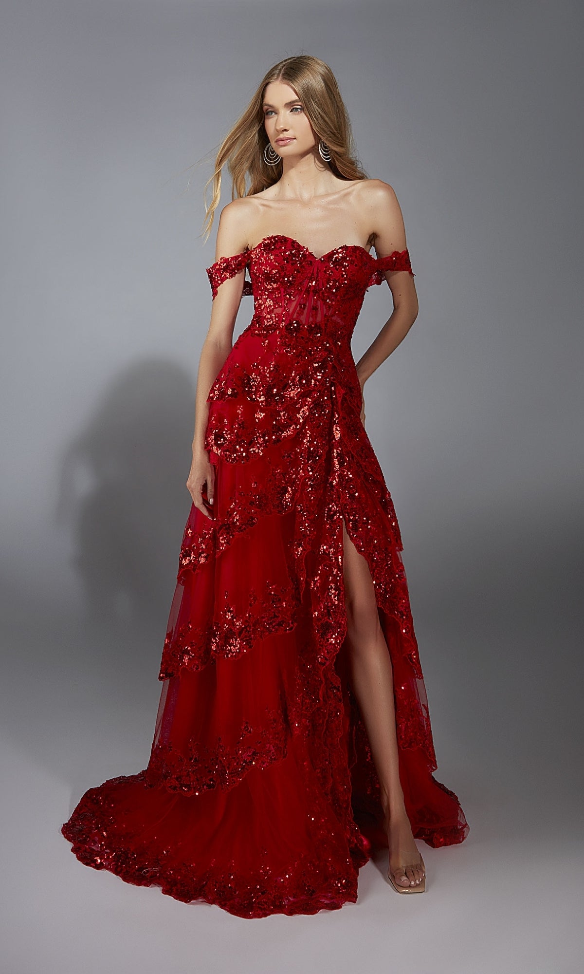 A woman stands against a plain gray background wearing the Aerie Couture 333 Long Prom Dress—strapless, off-the-shoulder with a corset bodice, red sequins, high slit, and layered tulle skirt.